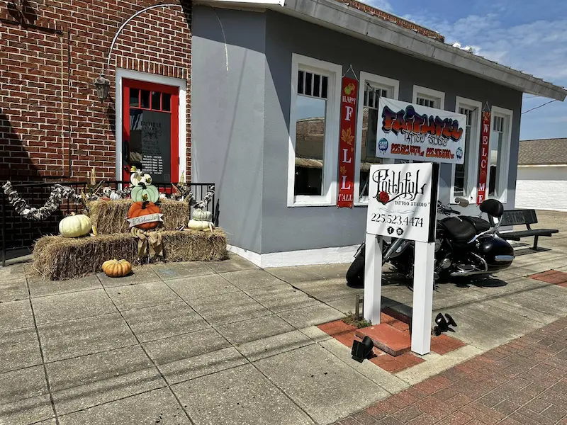 faithful tattoo studio exterior with red door autumn decor hay bales pumpkins. motorcycle by signage. happy fall yall banners